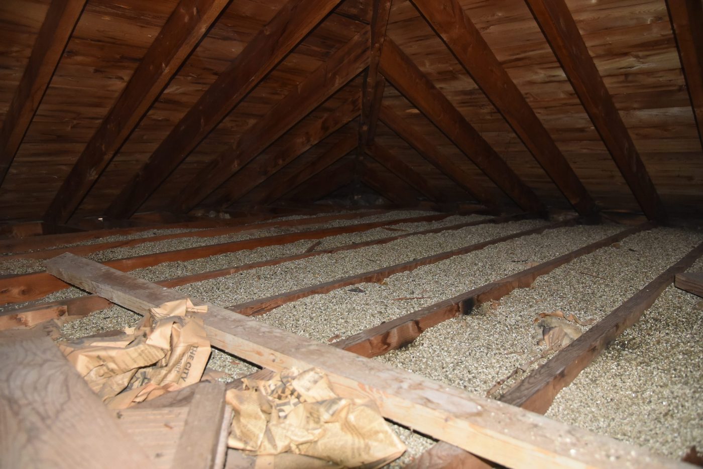 Vermiculite insulation between joists in an attic with old newspaper